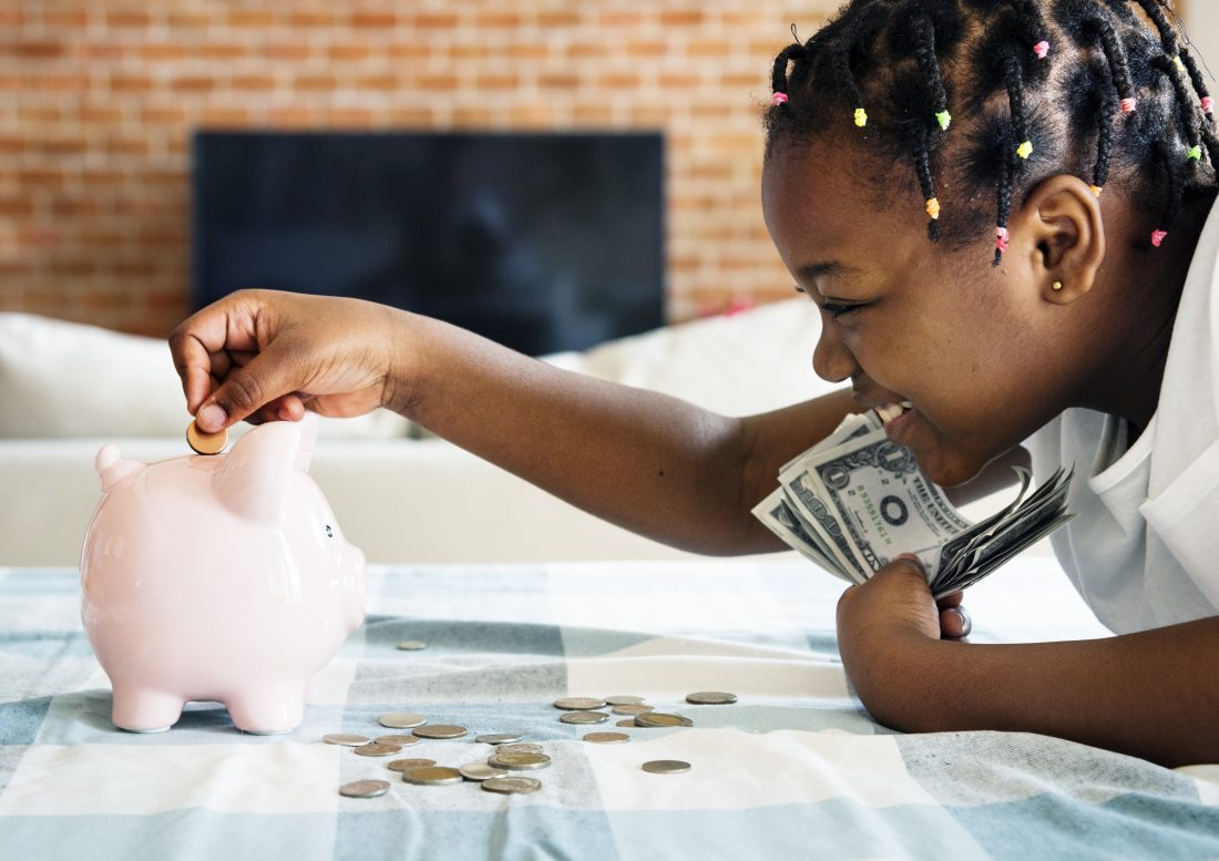 little girl putting money into her piggy bank